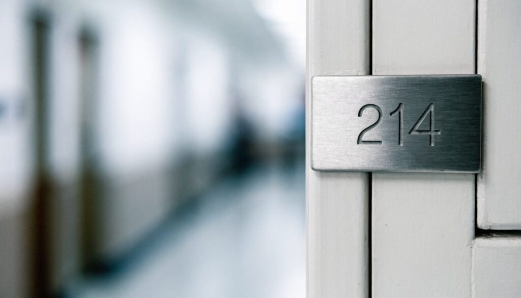 Plaque métallique gravée du numéro 214 fixée à côté de la porte d'une chambre, couloir flou en arrière-plan