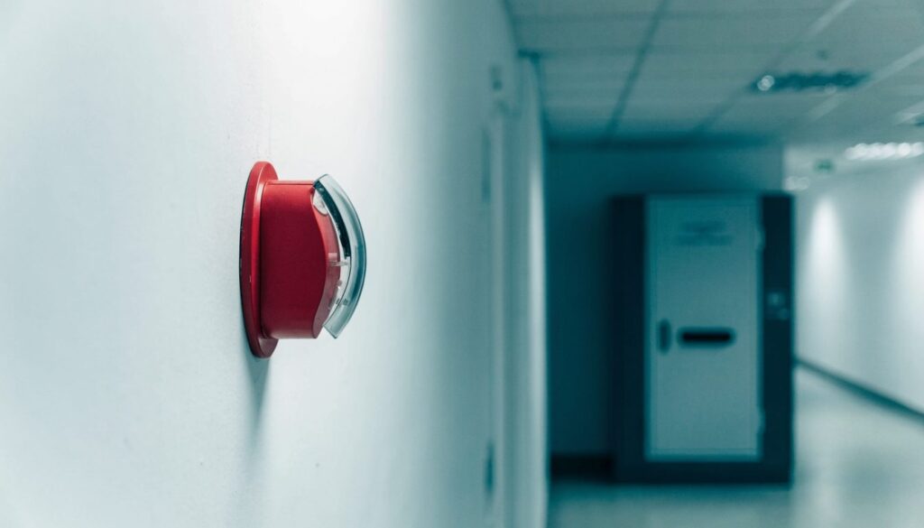 Déclencheur manuel d'alarme incendie rouge à membrane fixé sur un mur de couloir, armoire technique en arrière-plan